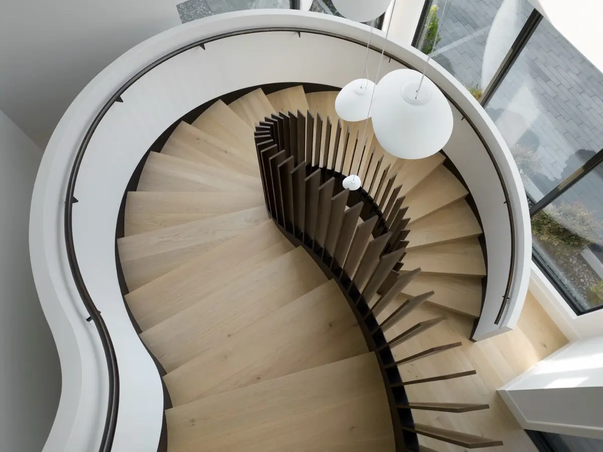 A spiral stair seen from above, oak treads inside a white balustrade
