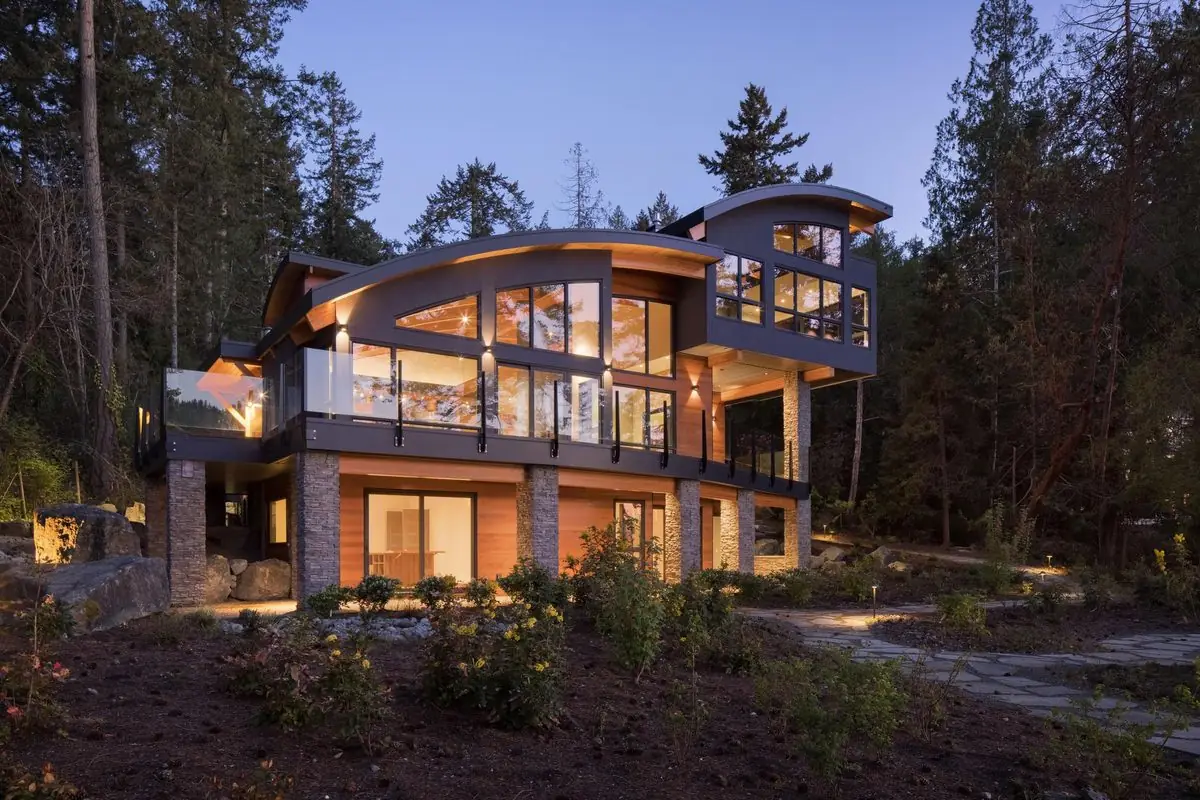 Curved glass home lit at dusk in the trees