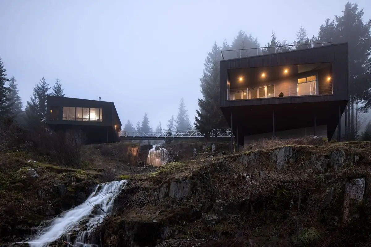 Black cabins above a waterfall in the mist