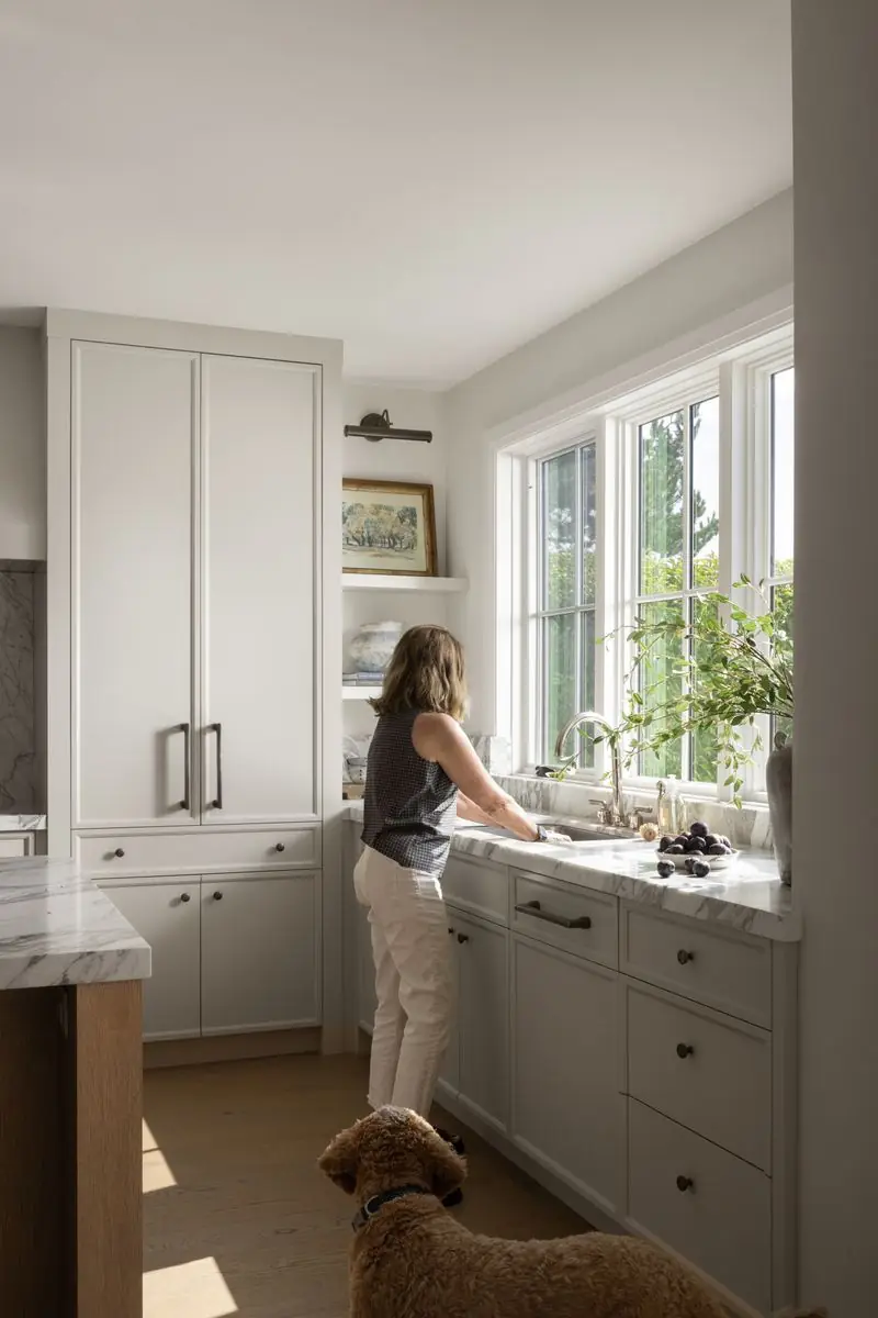 At the kitchen sink by the window, the dog close by