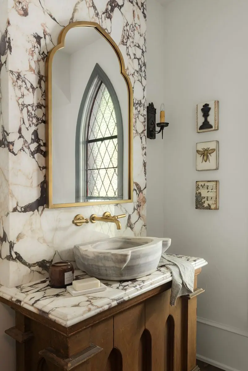 Powder room with a marble wall, a stone basin and an arched brass mirror