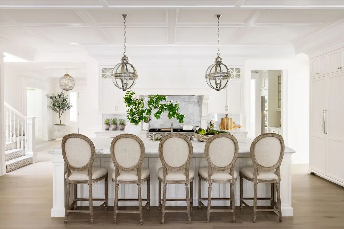 Five stools at a long white island under globe pendants