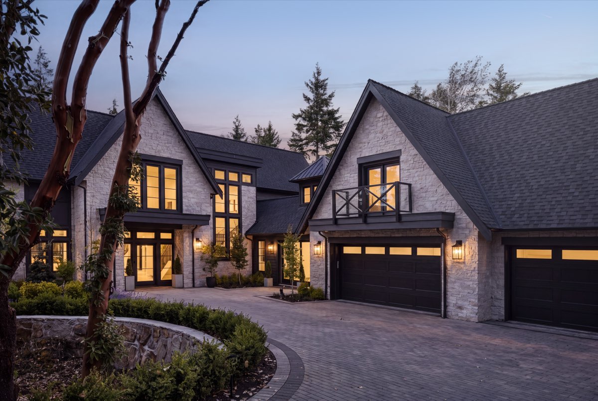 A shingled house at dusk behind an arbutus, its garage bays and windows lit warm.