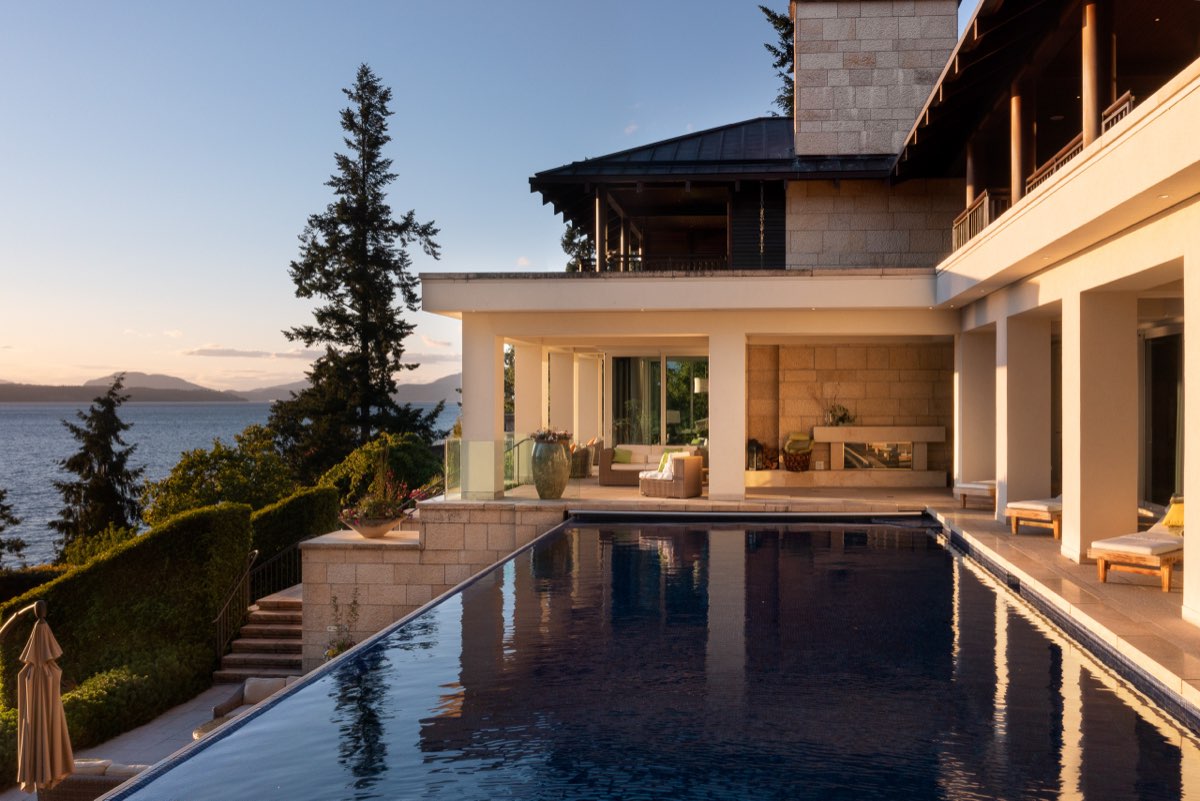 An infinity pool terrace at golden hour, the house open to the ocean