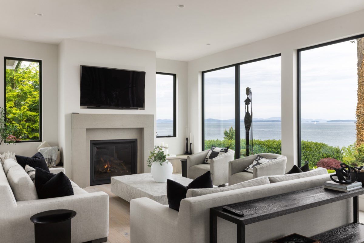 A pale living room with a low hearth and a long window to the water.